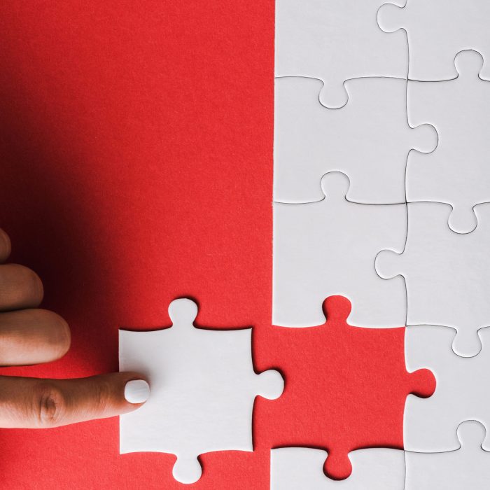 top view of woman pointing with finger at white jigsaw near connected puzzle pieces on red